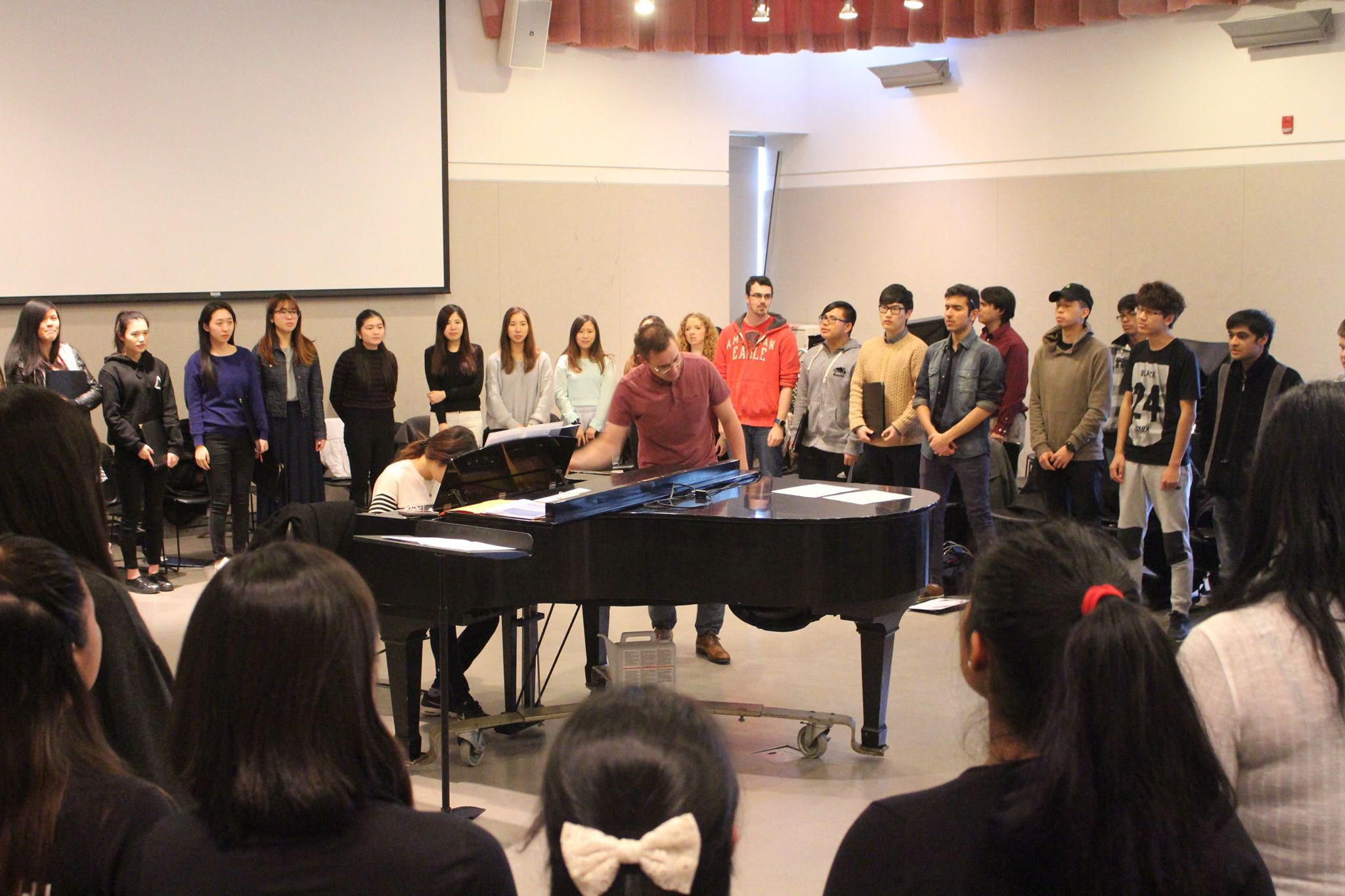 Participants are standing in a circle around a presenter and a musician playing the grand piano