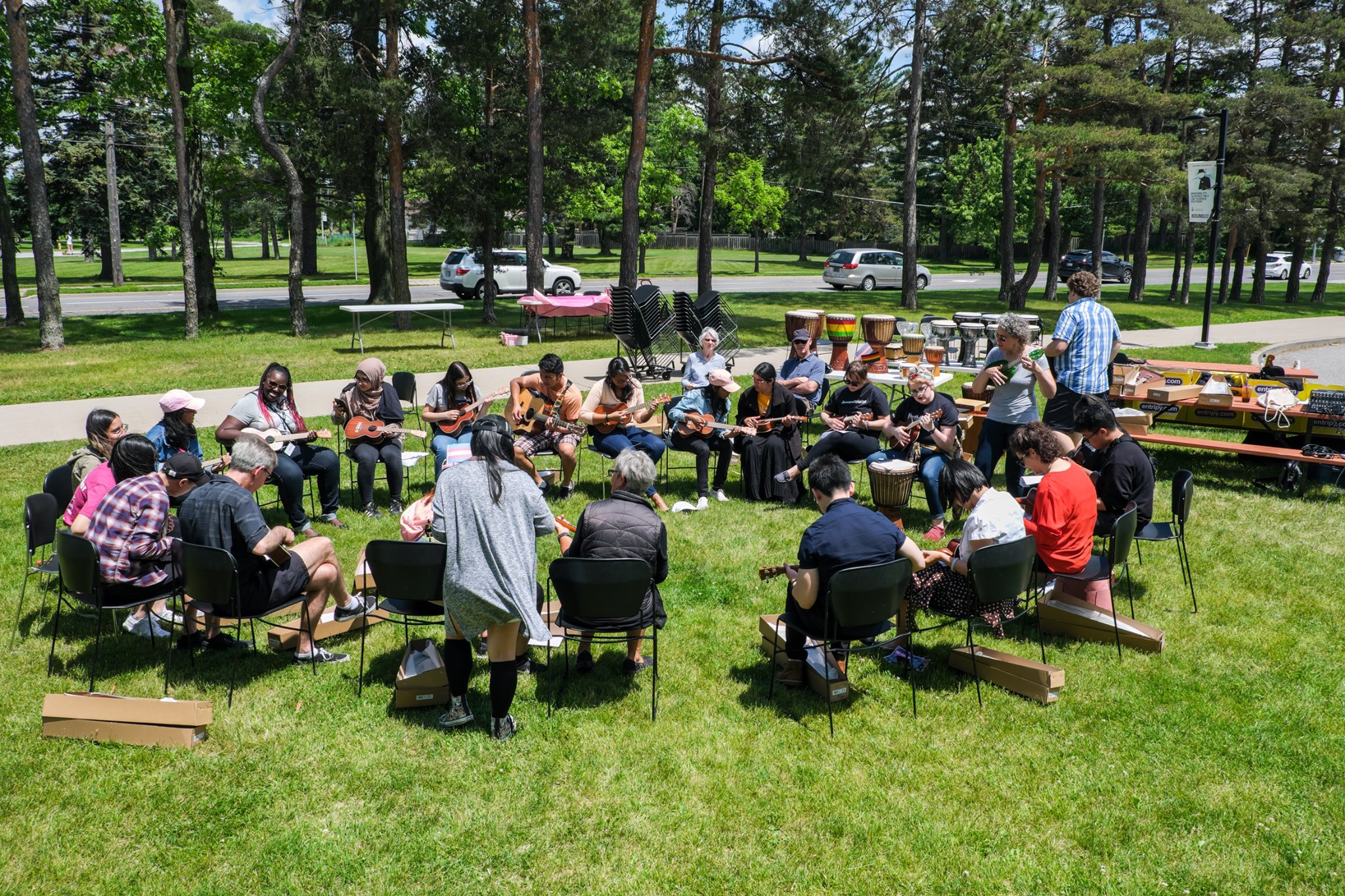 Participants sitting in a large circle on a field playing guitars and ukuleles