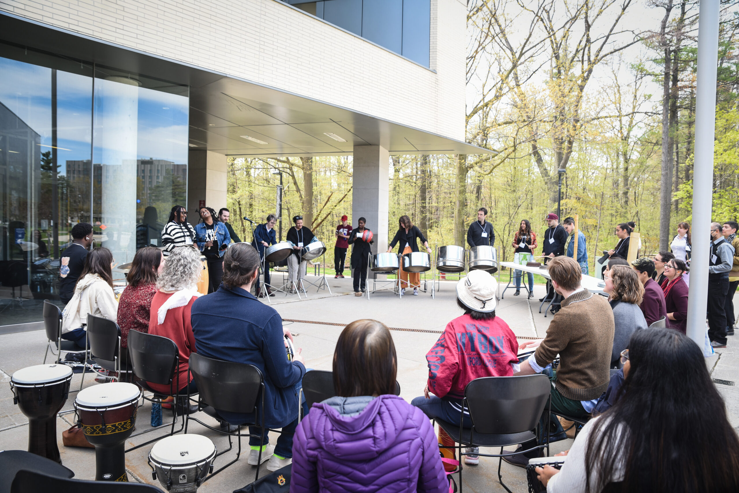 A circle of participants playing various instruments, including steel pans, hand drums and bells